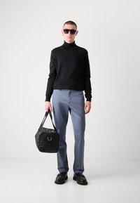 Suéter negro, pantalones azul claro, zapatos negros, sosteniendo un bolso negro con un acento plateado. Las gafas de sol completan el look. Diseño simple y moderno.