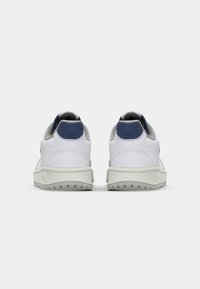 Zapatillas blancas con parte superior de cuero texturizado, acentos en azul marino en el talón y suela de goma gris con pequeños patrones de agarre.