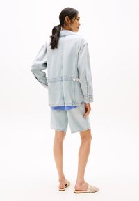 Ljusblå denim oversized-jacka med fyrkantig passform, tryckknappar på sidorna, bärs över en blårandig topp och ljus denimshorts.