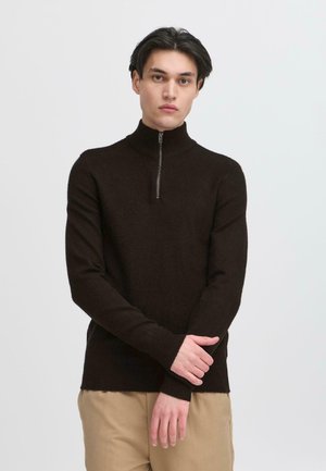 Pulover maro cu guler înalt și fermoar pe jumătate, având o textură moale și mâneci lungi, asortat cu pantaloni bej.