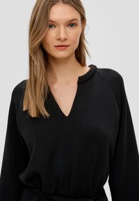 Czarny długi rękaw, top z głębokim dekoltem w kształcie litery V, o miękkiej fakturze i luźnym kroju. Posiada rękawy raglanowe oraz ściśnięty pas z kokardą.