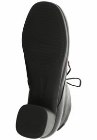 Suela de zapato de cuero negro con ranuras horizontales y un ligero tacón. Presenta un detalle de cinta en el lateral y una parte inferior texturizada para un mejor agarre.
