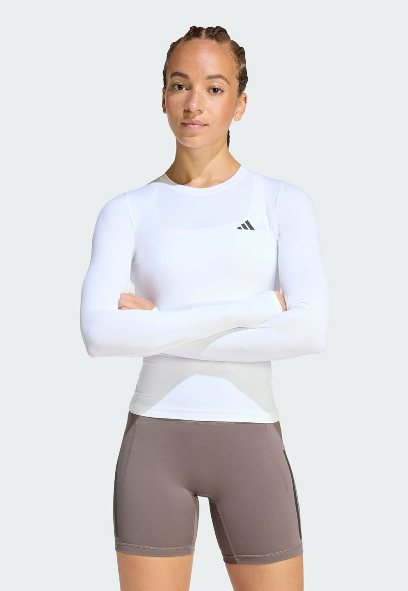 Λ ευκό αθλητικό πουκάμισο με μακριά μανίκια, στρογγυλή λαιμόκοψη και λογότυπο Adidas, σε συνδυασμό με καφέ σορτς με πλαϊνά διακοσμητικά στοιχεία. Ομαλή υφή υφάσματος.