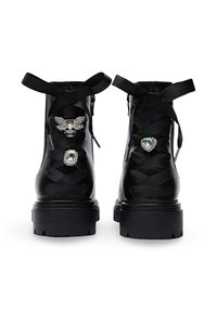 Bottines noires avec une semelle épaisse, ornées de lacets en satin et de décorations : une abeille et un cœur. Texture en cuir lisse.