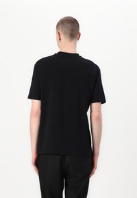 Μαύρο κοντομάνικο μπλούζα φτιαγμένο από βαμβάκι, με κλασικό λαιμό και χαλαρή εφαρμογή, με λεία υφή και χωρίς ορατά σχέδια.