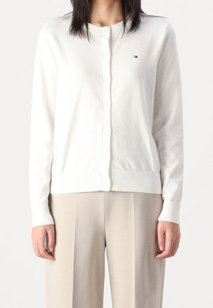 Cardigan blanc en tissu tricoté doux, avec un col rond, une fermeture à boutons et des poignets côtelés, arborant un petit logo sur la poitrine.
