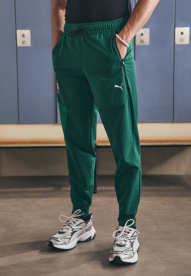 Gröna träningsbyxor med elastisk midja, sidofickor och en liten vit logotyp. I kombination med kraftiga silver- och svarta sneakers.