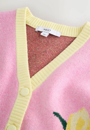 Rosa Cardigan mit gelbem Rippbesatz und Knöpfen, mit floralem Design. Der Stoff hat eine weiche Textur und ein kariertes Innenfutter.