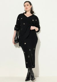 Abito maglione nero a maglia con scollo a V, caratterizzato da ritagli circolari, texture a coste e abbinato a un paio di stivali neri con tacco.