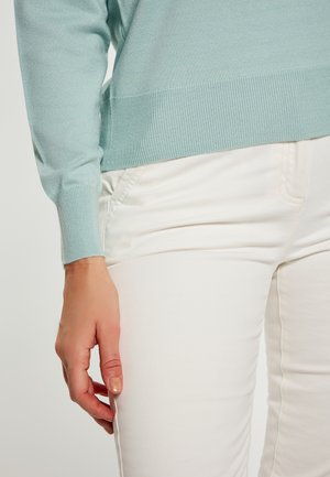Vaaleansininen neulepaita, jossa on ribbireunus ja hihansuut, yhdistetty valkoisiin slim fit -housuihin, joissa on sivutasku ja sileä pinta.