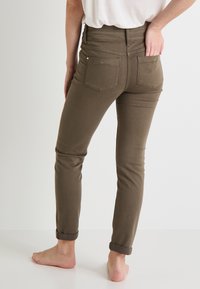 Vaqueros skinny marrones de cintura alta, con puños enrollados y dos bolsillos traseros. La tela parece suave y ligeramente elástica.