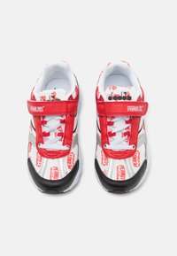 Zapatillas deportivas rojas y blancas que presentan gráficos de dibujos animados, una correa de velcro, paneles de malla y acentos de goma negra en la suela.