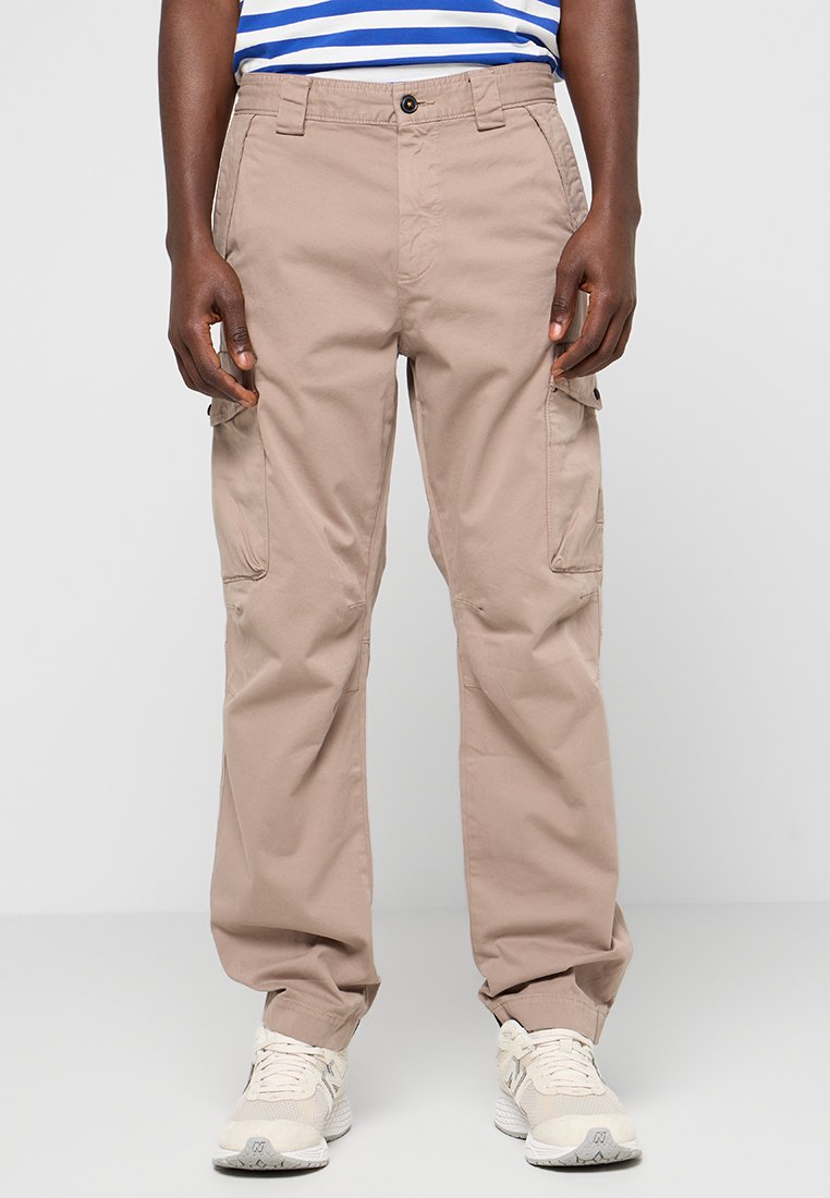 Beige cargobroek met zijzakken, gemaakt van lichte stof. Ruime pasvorm met een recht model. Gedragen met witte sneakers.