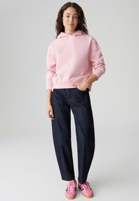 Felpa rosa con polsini a costine, pantaloni in denim scuro con taglio dritto e sneakers rosa con superficie strutturata e lacci.