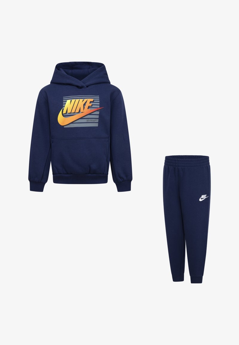 Conjunto de hoodie e calças de treino em azul marinho, feito de tecido macio; possui um bolso frontal e um logo da Nike proeminente em amarelo e laranja no hoodie.