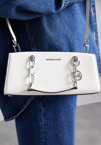 Valkoinen Michael Kors -käsilaukku, jossa on hopeiset ketjuakcentit, käytössä sinisen farkkutakin ja farkkujen päällä.