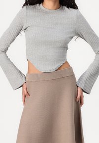 Maglietta grigia a maniche lunghe con righe e orlo curvo, abbinata a una gonna marrone con vita in maglia, che mostra una texture liscia e un design aderente.