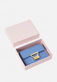 Billetera de cuero azul con un acabado texturizado, que presenta un cierre dorado y una caja rosa con lettering dorado.
