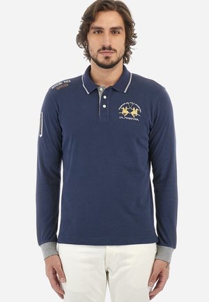 Marineblå langærmet polo skjorte med grå krave og manchetter. Har broderede logoer og et badge på ærmet. Fremstillet af bomuldsmateriale.
