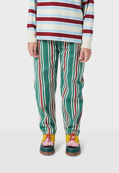 Camisa de manga larga a rayas en crema, azul y marrón; pantalones de pana verdes con rayas verticales rojas y blancas; zapatos multicolores con flecos.