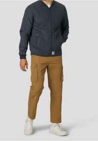 Marinblå quiltad bomberjacka med dragkedjestängning, ribbad manschetter och midja. I kombination med tanfärgade cargobyxor som har flera fickor och en texturerad yta.