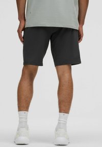 Mørkegrå shorts med et glat, let stof, der har elastisk talje og når midt på låret, parret med hvide sportsko og sokker.