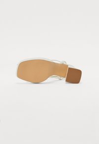 Witte hoge sandaal met een open achterkant, met een glad bovenwerk en een gestructureerde rubberen zool. Vierkante hak en slanke banden voor ondersteuning.