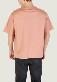 Camiseta de manga corta de color rosa claro con cuello redondo y corte holgado, combinada con vaqueros de color gris oscuro. Tela simple y lisa sin patrones visibles.