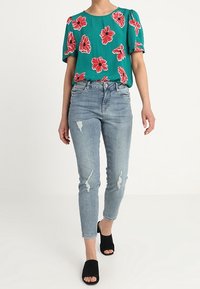 Tyrkysová květinová blůza s nafouknutými rukávy, spárovaná s světle modrými zničenými skinny džíny a černými otevřenými mules.
