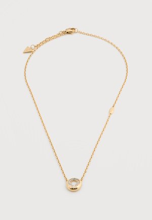 Collier délicat en chaîne d'or avec pendentif circulaire orné de petites pierres claires autour d'un centre creux sur un fond uni.