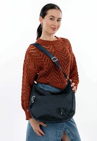 Borsa a spalla in rete nera con logo ricamato "SFY", dotata di zip argentata e tracolla regolabile, abbinata a un maglione a righe color ruggine.