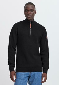 Svart zip-up genser med høy krage, ribbede mansjetter og hem, med en kontrasterende glidelåsdrager og logo detaljer på ermet.