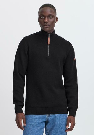 Schwarzer Reißverschluss-Pullover mit hohem Kragen, gerippten Bündchen und Saum, ausgestattet mit einem kontrastierenden Reißverschluss-Anhänger und Logo-Detail auf dem Arm.