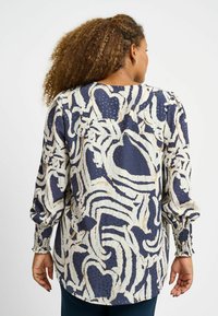 Blusa a maniche lunghe con un motivo astratto navy e crema, tessuto testurizzato e polsini arricciati. La vista posteriore mostra una vestibilità rilassata.