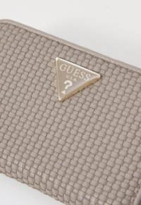 Woven gray synthetic material wallet with a triangular gold logo plaque featuring "GUESS U.S.A." and a question mark design.