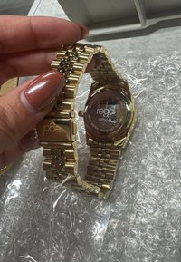 Gold watch with a stainless steel case and band, featuring a linked design. Display side shows a clear glass front and detailed back.