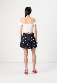 Fehér, váll nélküli crop top, amely egy tengerészkék szoknyával van párosítva, amely fehér pöttyökkel, réteges fodor kialakítással rendelkezik, és piros magassarkú szandálokkal.