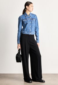 Džínová bunda má priliehavý strih, svetlomodrú farbu, strieborné gombíky a náprsné vrecká. Kombinovaná s širokými čiernymi nohavicami a malou čiernou taškou.