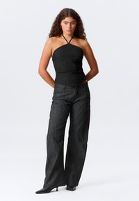 Musta halterneck-top, jossa on teksturoidut kankaat, yhdistettynä löysiin, korkeavyötäröisiin mustiin housuihin, joissa on hienovarainen pystysuuntainen kuosi.