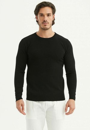 Un pull noir à manches longues en fine maille avec un col rond. Associé à un pantalon de couleur claire, présentant une coupe classique.