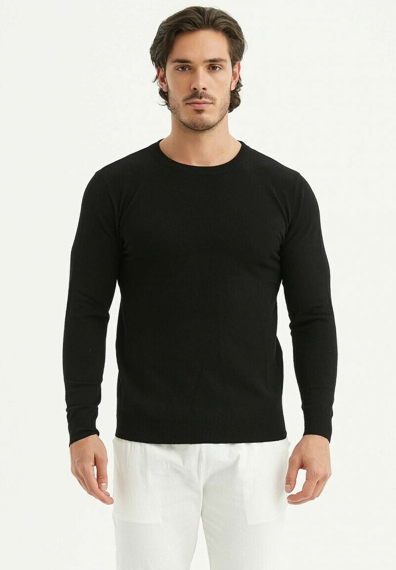 Un pull noir à manches longues en fine maille avec un col rond. Associé à un pantalon de couleur claire, présentant une coupe classique.