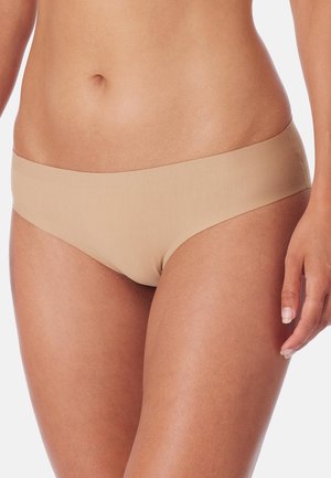 Torace e parte superiore delle gambe di una donna che indossa biancheria intima beige liscia e senza cuciture, con la mano destra visibile e pelle dal tono uniforme.