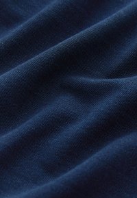 Gros plan d'un tissu bleu foncé avec des plis doux, montrant une texture tissée fine et des reflets subtils de lumière.