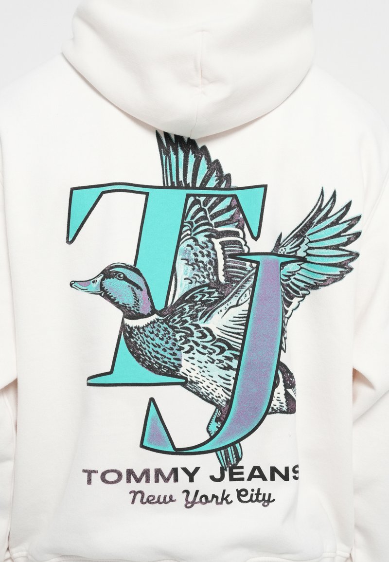 Weißer Kapuzenpullover mit einer großen Grafik eines Enten neben den Buchstaben "TJ" in Teal und Lila. Der Text lautet "TOMMY JEANS New York City."