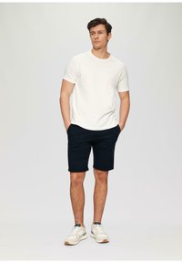 Conjunto de camiseta blanca de manga corta y pantalones cortos azul marino, con un corte relajado. El modelo lleva zapatillas ligeras con detalles en negro. Sin patrones ni gráficos.