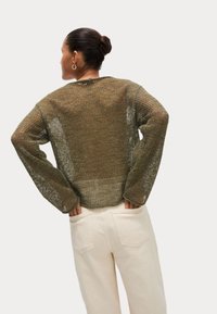 Pull en tricot vert olive à coupe ample, avec des manches larges et un motif texturé, associé à un pantalon taille haute de couleur claire.