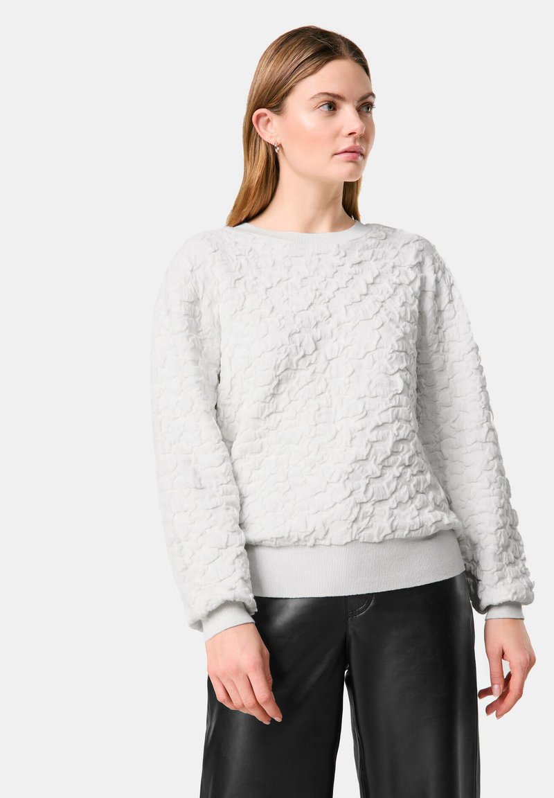 Helles graues Sweatshirt mit strukturierter, rauer Oberfläche, Rundhalsausschnitt und gerippten Bündchen, kombiniert mit schwarzen Lederhosen.