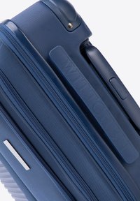 Námořnický hardshell kufr s texturovaným povrchem, zipovými přihrádkami a embosovaným logem značky na boku. Odolný materiál a zvýrazněné detaily.