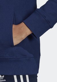 Merinovärinen collegepaita med ribbade ärmslut och en ficka fram, tillverkad av texturerad tyg. Inkluderar en diskret logotyp i botten.