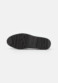 Semelle de chaussure noire avec des motifs de grip texturés et le nom de la marque "Tamaris" embossé près du talon, taille 37 marquée.